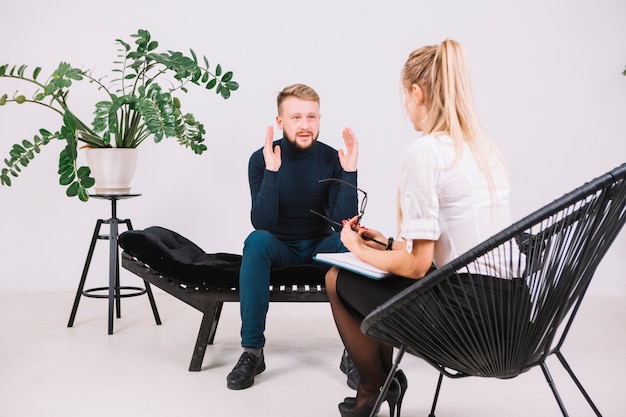 Young man sitting on couch discussing with female psychotherapist his problems