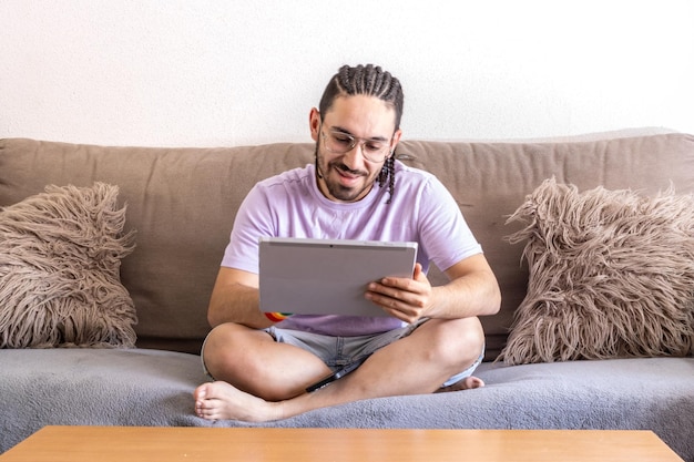 A young man sitting on the couch using his digital tablet Front view of man sitting in the living room using his tablet Smiling man touching digital tablet sitting in room