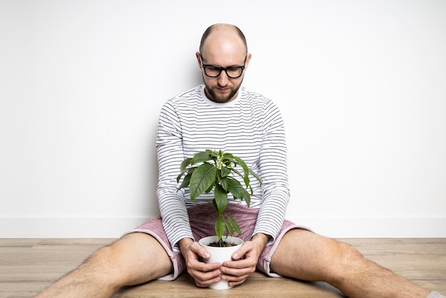 Young man sitting on the floor holding an indoor flower in a pot