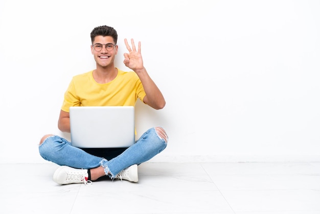 Young man sitting on the floor isolated on white background happy and counting three with fingers