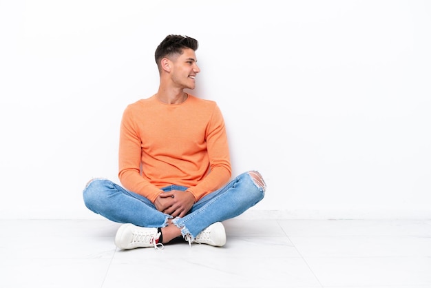 Photo young man sitting on the floor isolated on white background looking side