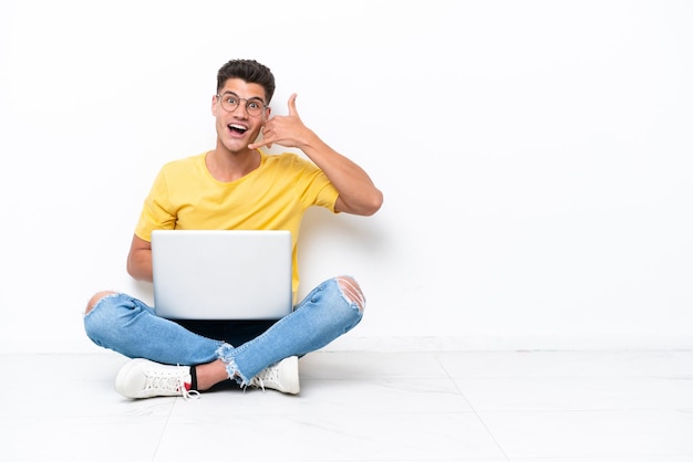 Young man sitting on the floor isolated on white background making phone gesture Call me back sign