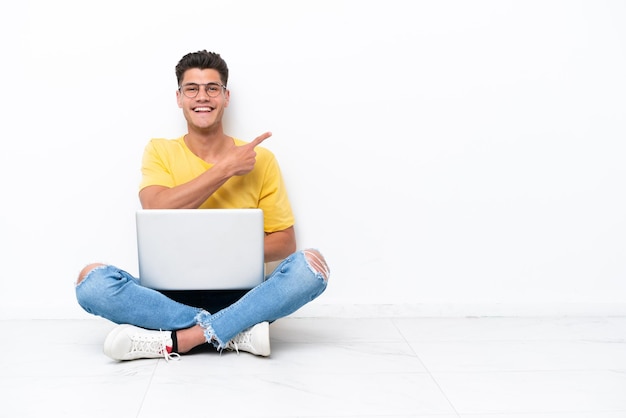 Young man sitting on the floor isolated on white background pointing to the side to present a product