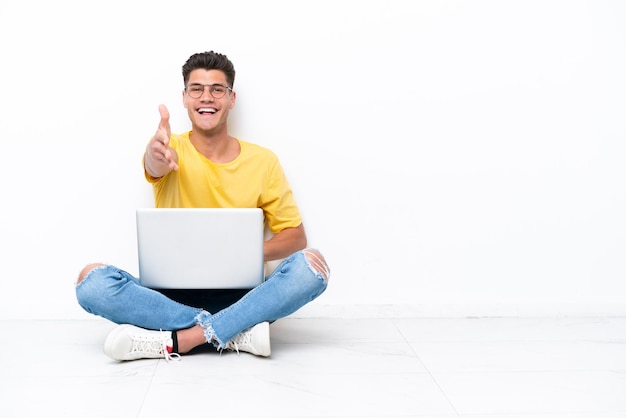 Young man sitting on the floor isolated on white background shaking hands for closing a good deal