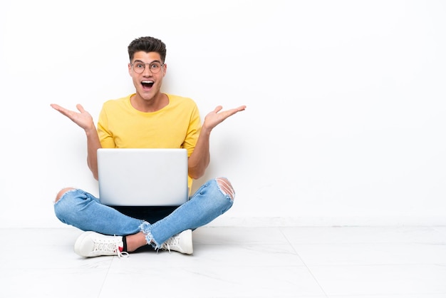 Young man sitting on the floor isolated on white background with shocked facial expression