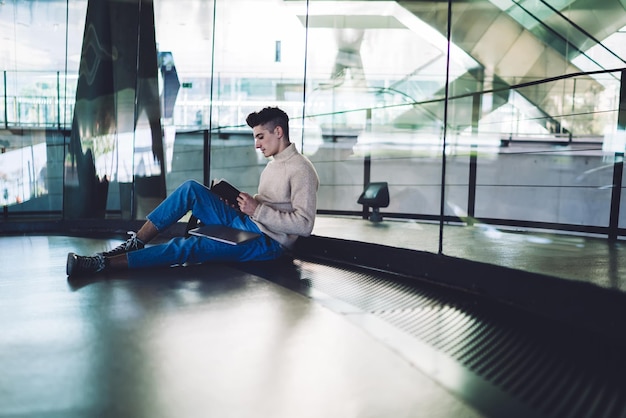 Young man sitting on floor and reading notebook