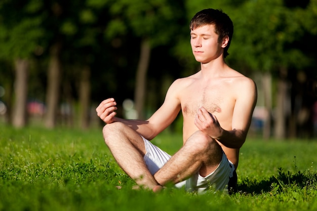 Young man sitting on green grass and meditating