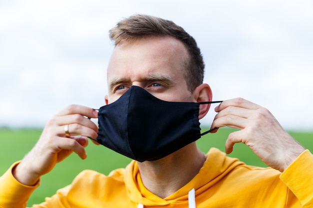 Young man sitting on green grass in a protective antiviral mask and thinking about the future. The guy is resting in the park on a sunny summer day. The concept of rest. Virus protection. Quarantine