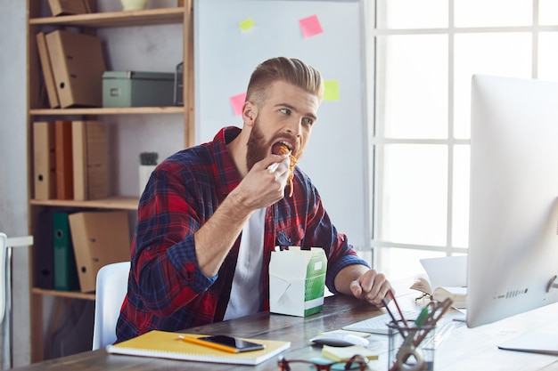 Young man sitting at office table and having lunch break