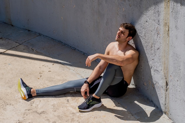 Young man sitting resting after training sunbathing without shirt