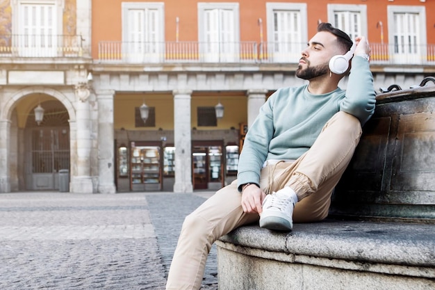 young man sitting on the street listening to music with wireless headphones