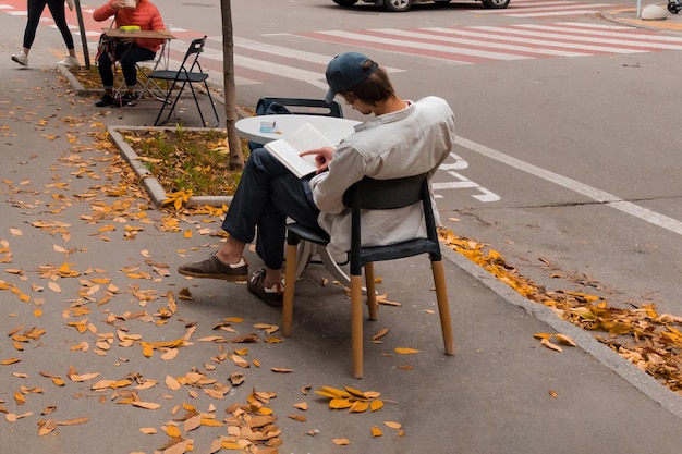 Young man sitting at the table near a road on the sidewalk and reading a book Cafeteria Caucasian Drinking Modern Young Attractive Cheerful Coffee Academic Achievement Client Customer