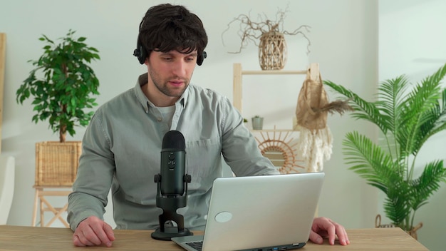 Young man sitting at table with laptop talking on mic