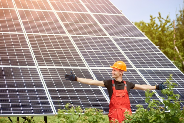 Young man smiles with arms open against the background of solar panels he satisfied his work