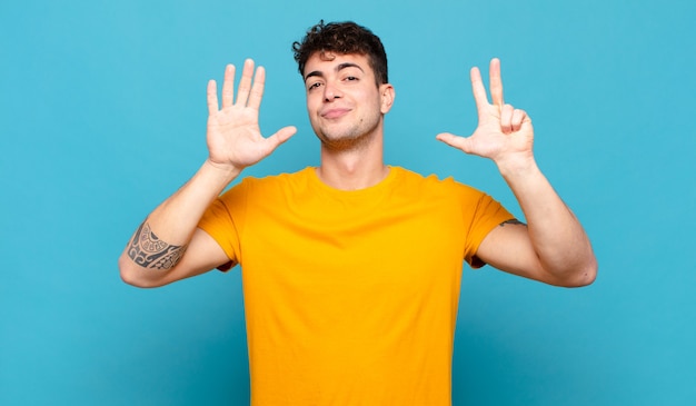 Young man smiling and looking friendly, showing number eight or eighth with hand forward, counting down