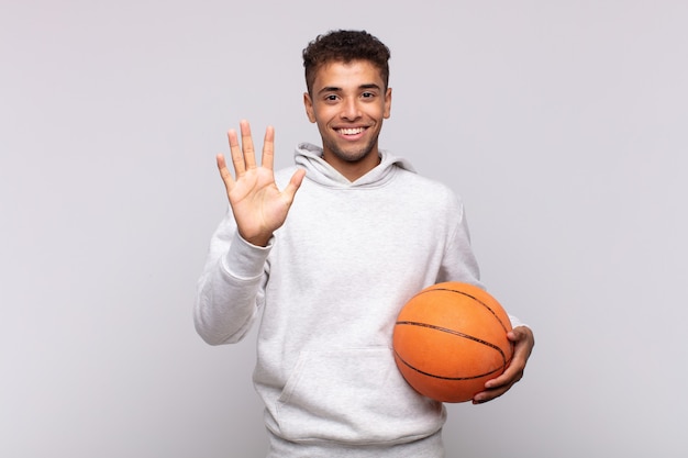 Young man smiling and looking friendly, showing number five or fifth with hand forward, counting down. basket concept