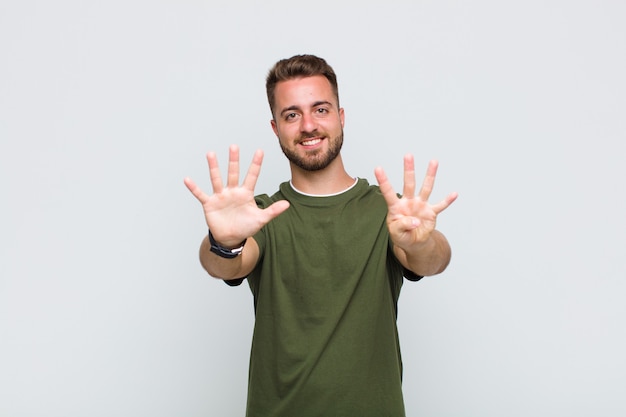 Young man smiling and looking friendly, showing number nine or ninth with hand forward, counting down