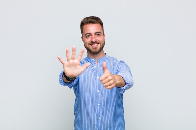 Young man smiling and looking friendly, showing number six or sixth with hand forward, counting down