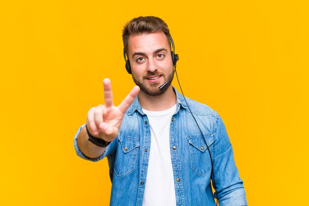 Young man smiling and looking happy, carefree and positive, gesturing victory or peace with one hand