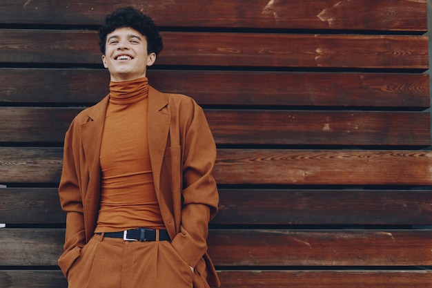 Photo young man smiling in a stylish orange outfit against a wooden background