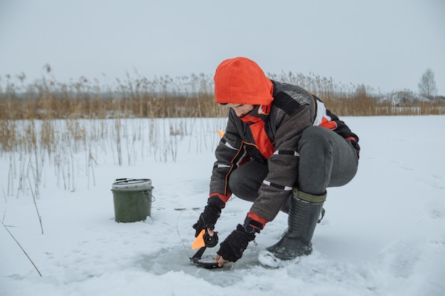 Young man on a snowy lake winter fisherman sets bait