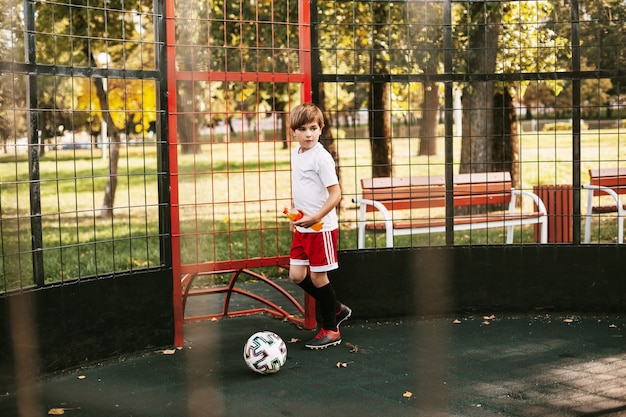 A young man in a sports uniform trains with a ball on the freestyle football court.