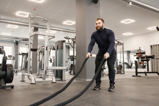 Young man in sportswear doing excercisses with special rope at gym