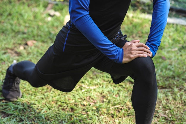 Young man in sportswear doing a warm-up on the green grass sports ground