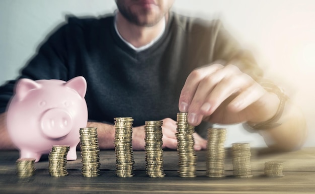 young man behind stacked coins and a piggy stacks coins to it to save his money. ideal for websites and magazines layouts