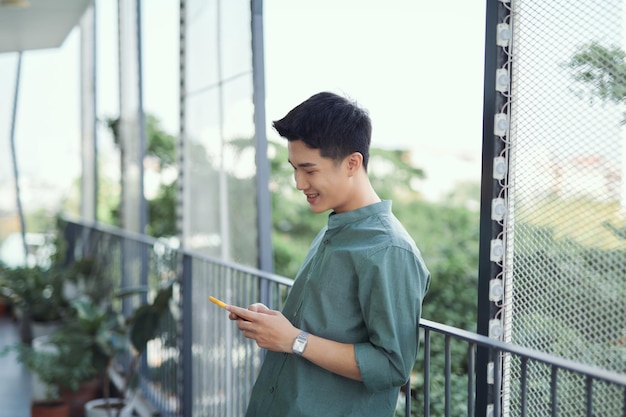 Young man standing on balcony texting on mobile phone