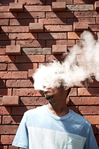 Young man standing by red brick wall on sunny day and smoking