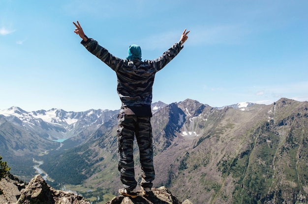 A young man standing on a hill with raised hands freedom The tourist has conquered the top of the mountain