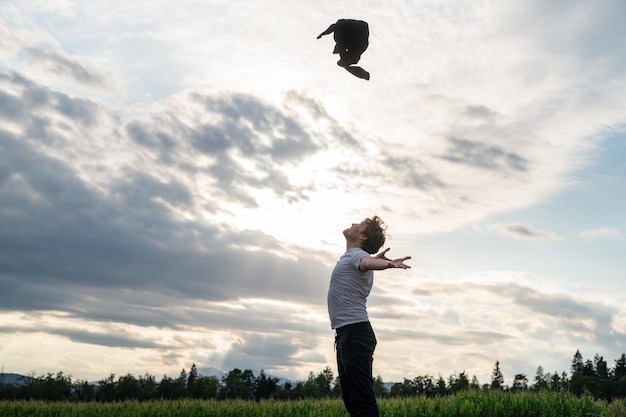 Young man standing in nature under beautiful evening sky throwing his sweater high up in the