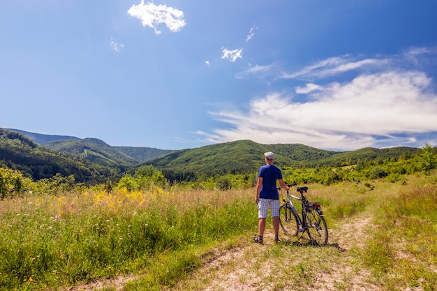 Young man standing near  bicycle in morning sunrise with wonderful rays and morning mist during calm summer active day