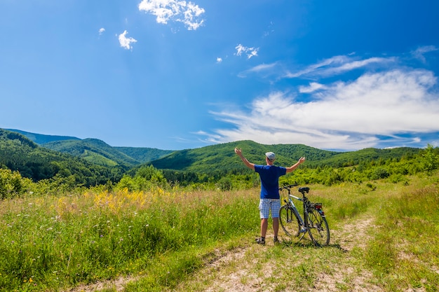 Young man standing near  bicycle in morning sunrise with wonderful rays and morning mist during calm summer active day