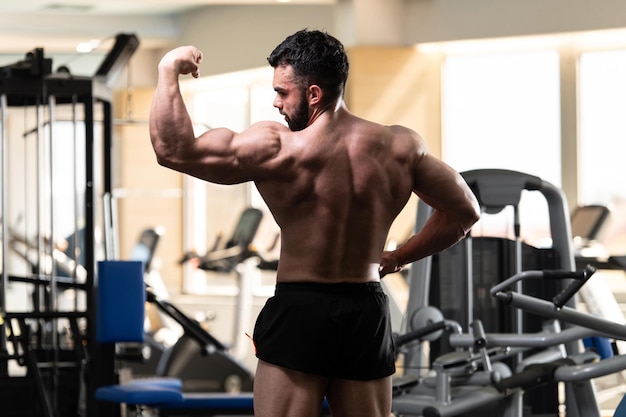 Young Man Standing Strong In The Gym And Flexing Muscles Muscular Athletic Bodybuilder Fitness Model Posing After Exercises