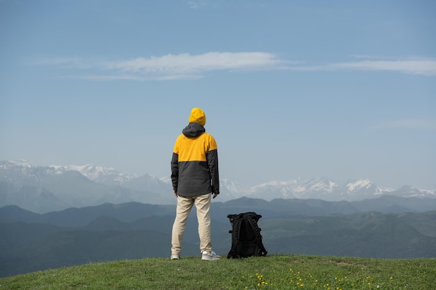 Young man standing on the top of the mountain enjoying scenic view of snowy peaks of mountain range