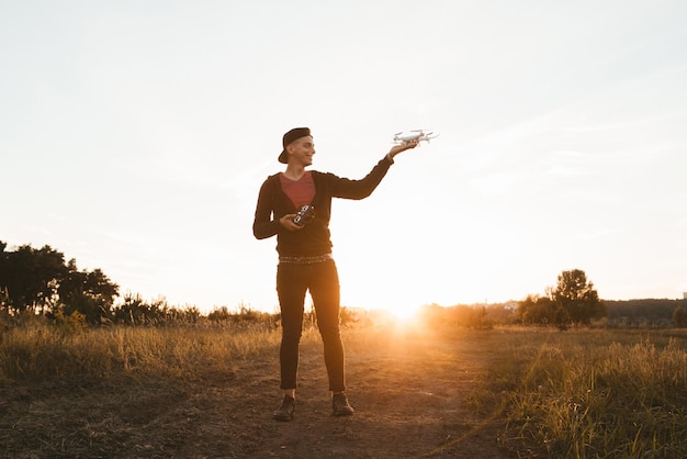 Young man standing with drone outdoor sunset flare Presentation of unmanned aerial vehicle at nature successful landing to hand by remote controller