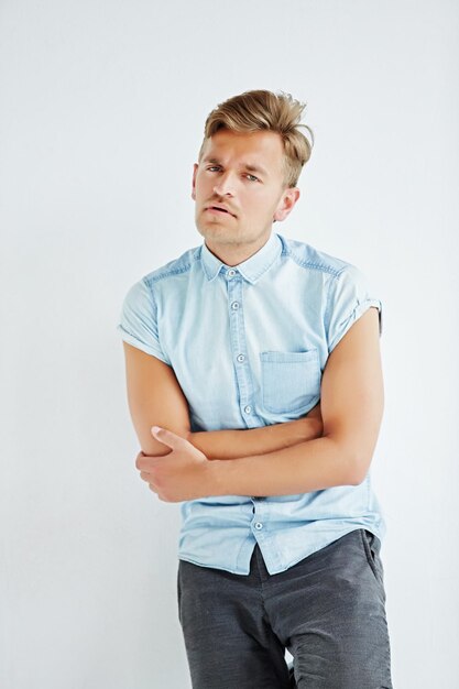 Young man standing with hands clasped in front of him leaning against the white wall