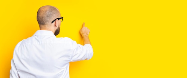 Young man standing with his back pointing his finger at an invisible screen on a yellow background Banner