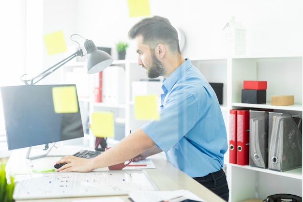 A young man stands in the office near a transparent Board with stickers.