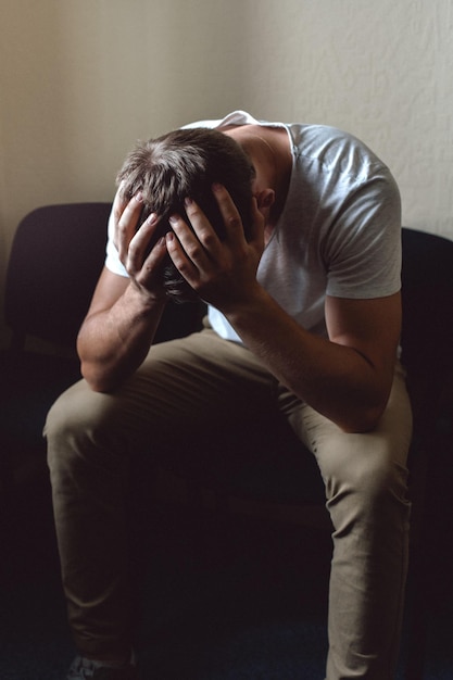 A young man in a state of crisis and despair The white guy is sitting on a chair and holding his head with his hands