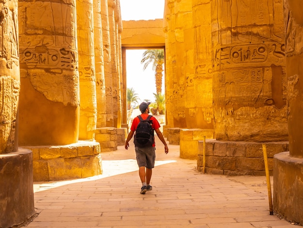 Photo young man strolling between the hieroglyphic columns of the temple of karnak, egypt