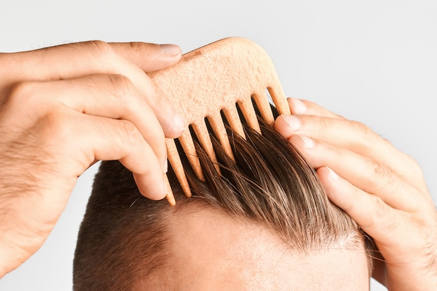 Young man styling his hair with a wooden comb. Hair styling at home. Advertising concept of shampoo for healthy hair and against dandruff.