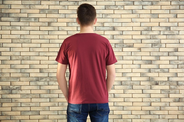 Young man in stylish tshirt on brick wall background Mockup for design