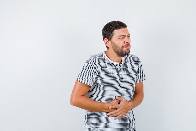 Young man suffering from stomach pain in t-shirt and looking bothered , front view.