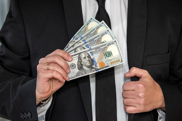 Young man in suit putting dollar bills in his pocket Concept of bribery or corruption