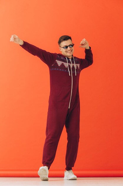 A young man in sunglasses and a Christmas kigurumi dances on a red background