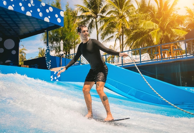 Young man surfing on a wave simulator at a water amusement park