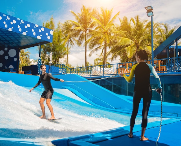 Young man surfing with trainer on a wave simulator at a water amusement park